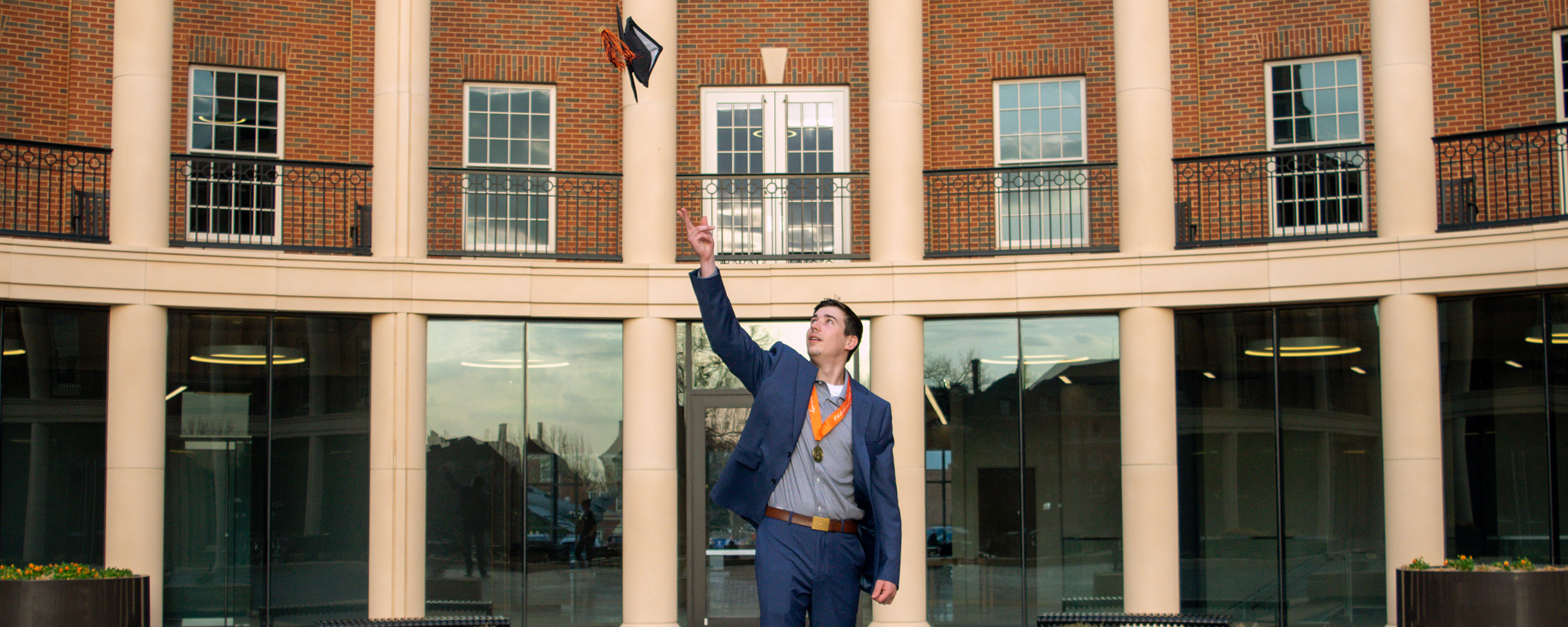 Student throwing cap in front of the Business Building