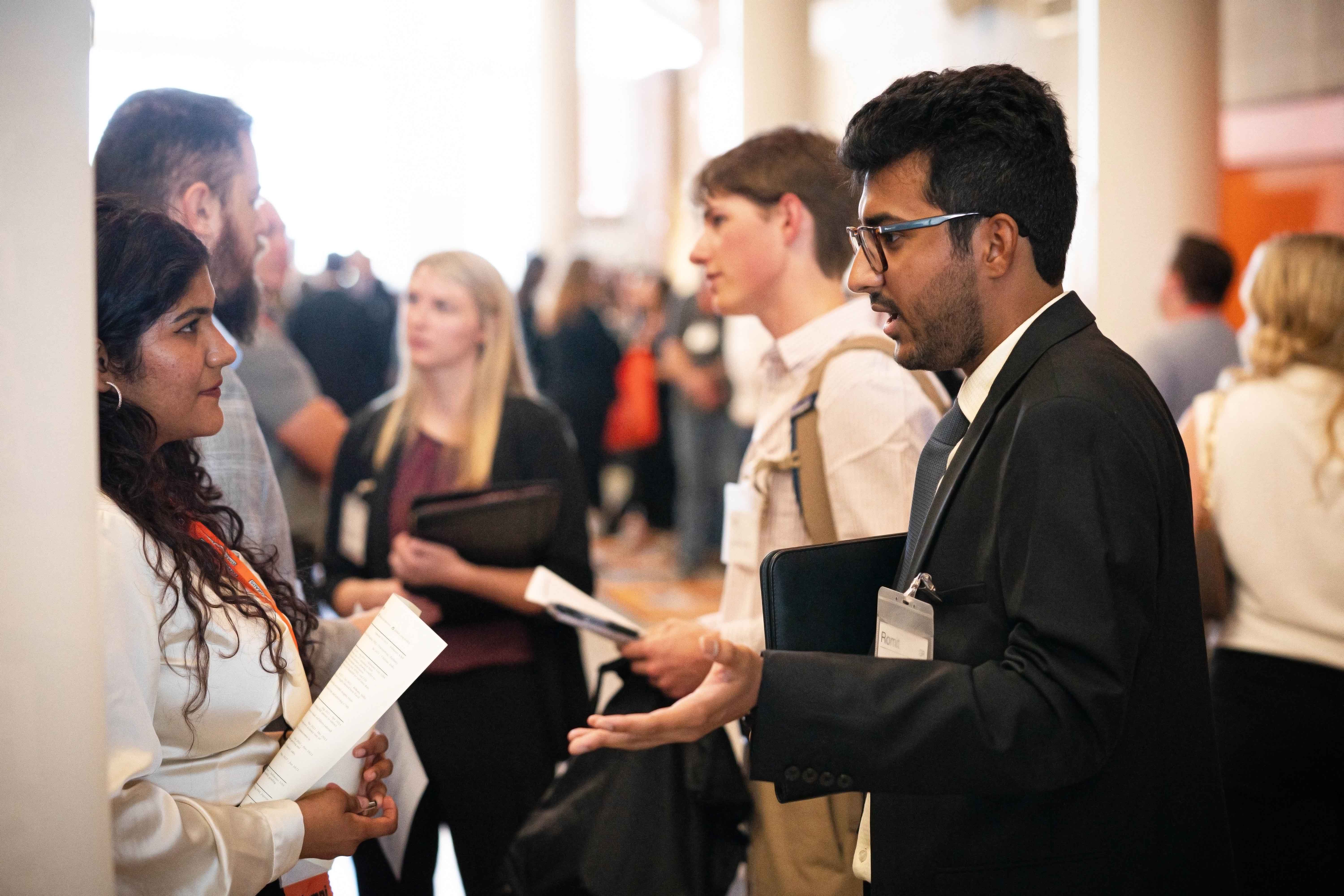 Male student dressed professionally speaking to a potential employer at a career fair