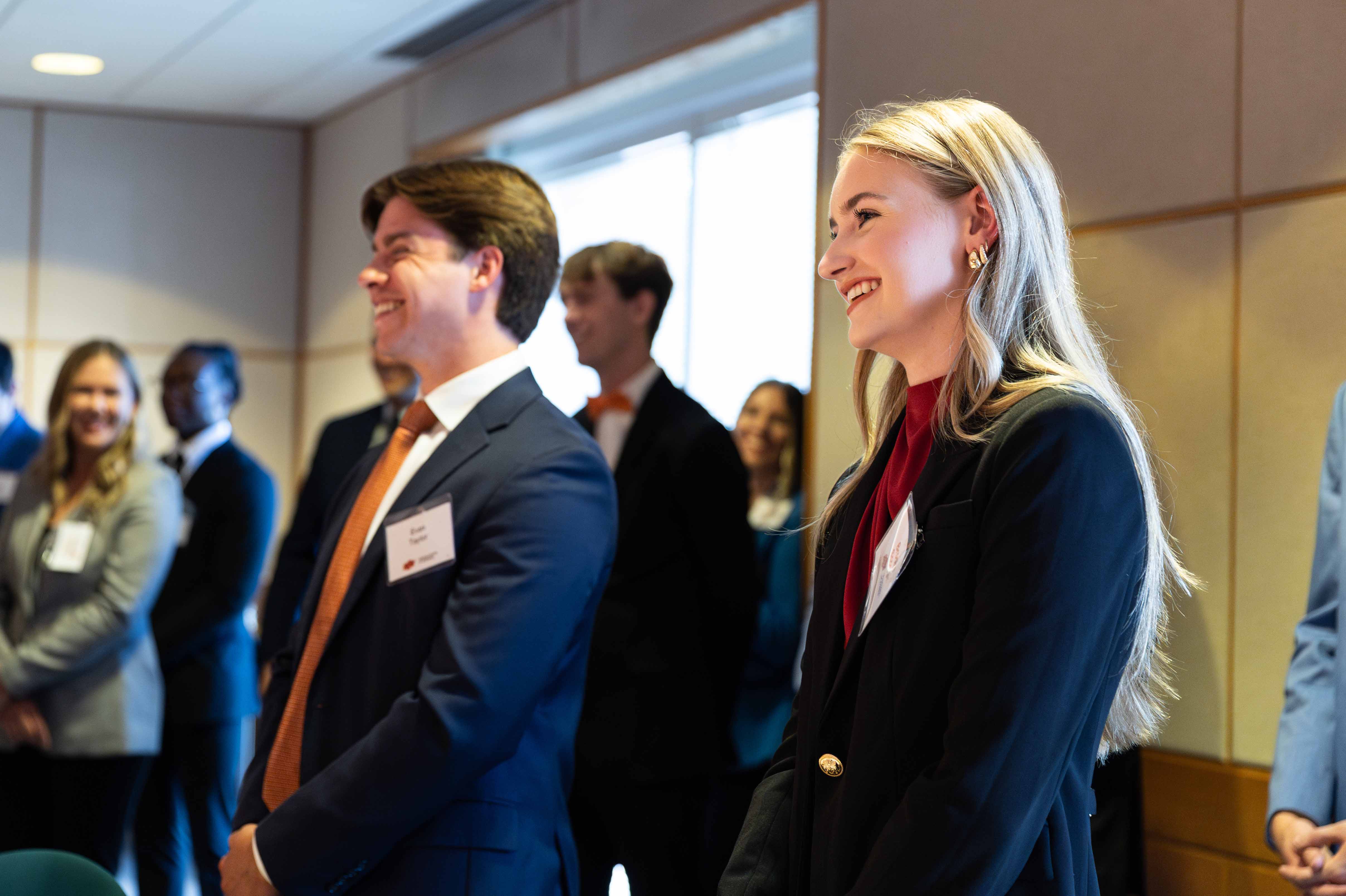 A male and female student wearing business professional clothing and smiling.