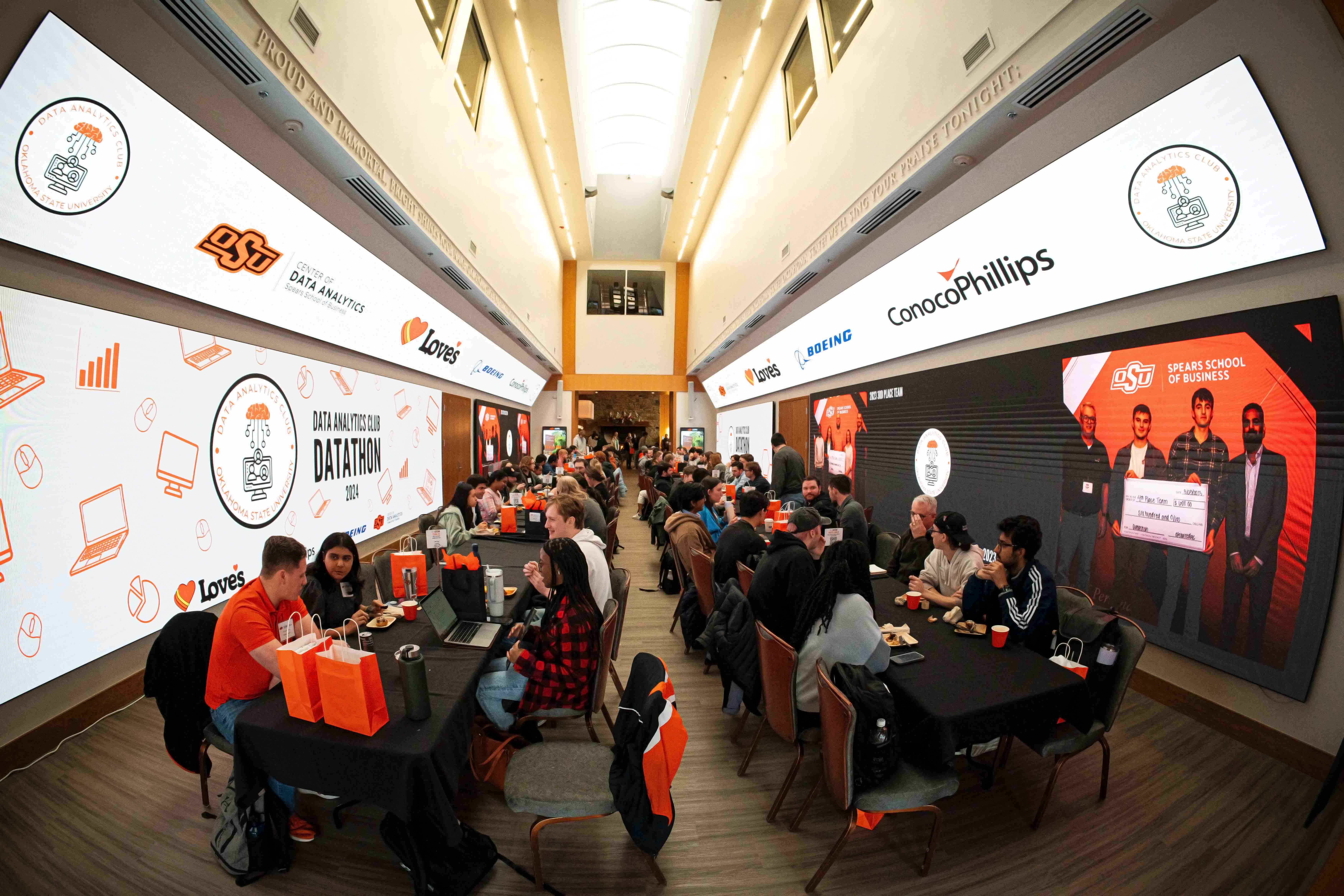 Students sitting in groups in the Alumni Center for the Datathon event. Groups are working on their projects for the competition. Each student group has an industry advisor sitting with them.