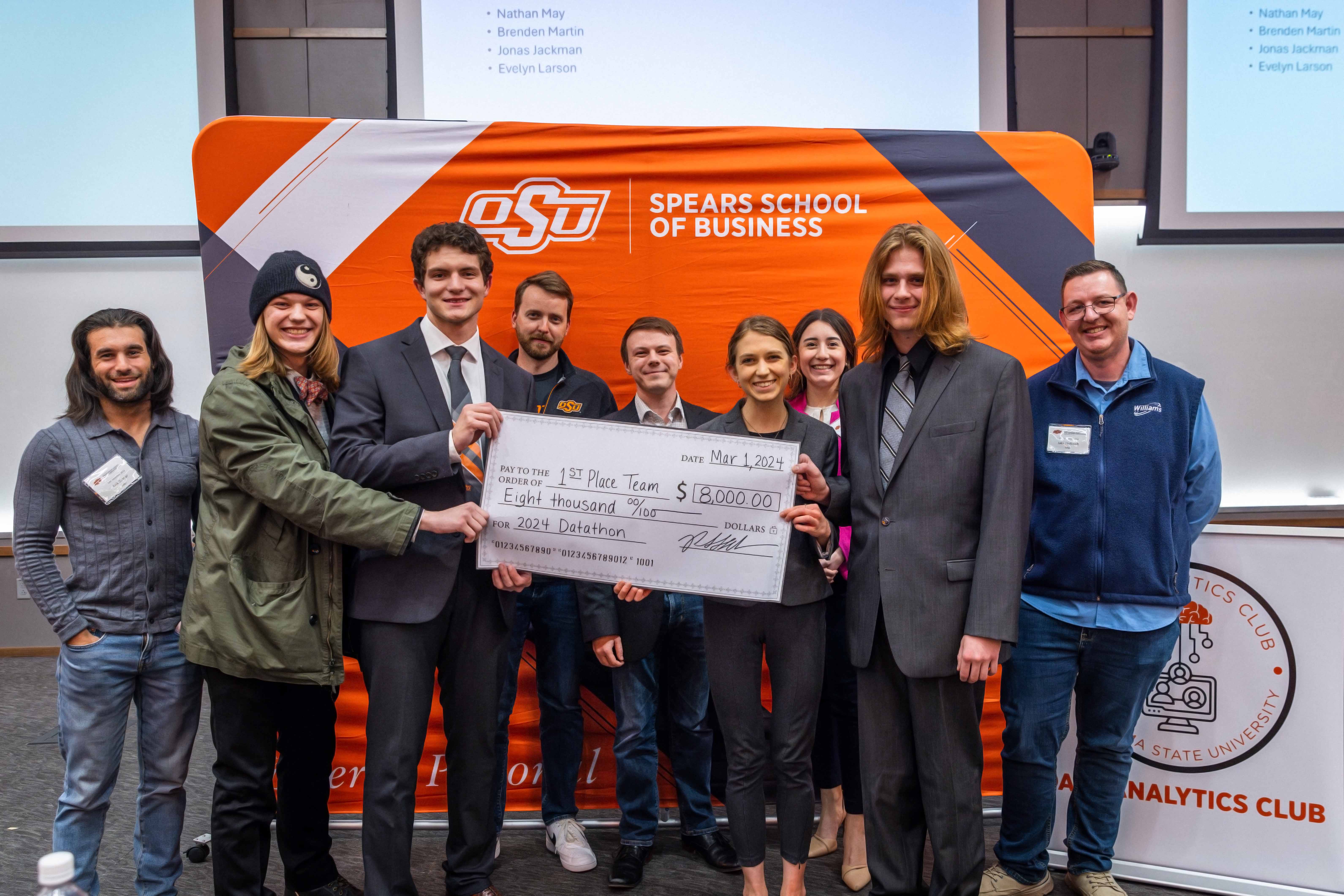 Winners of the datathon competition holding a check for $8,000. Group of 8 students and their industry advisor.