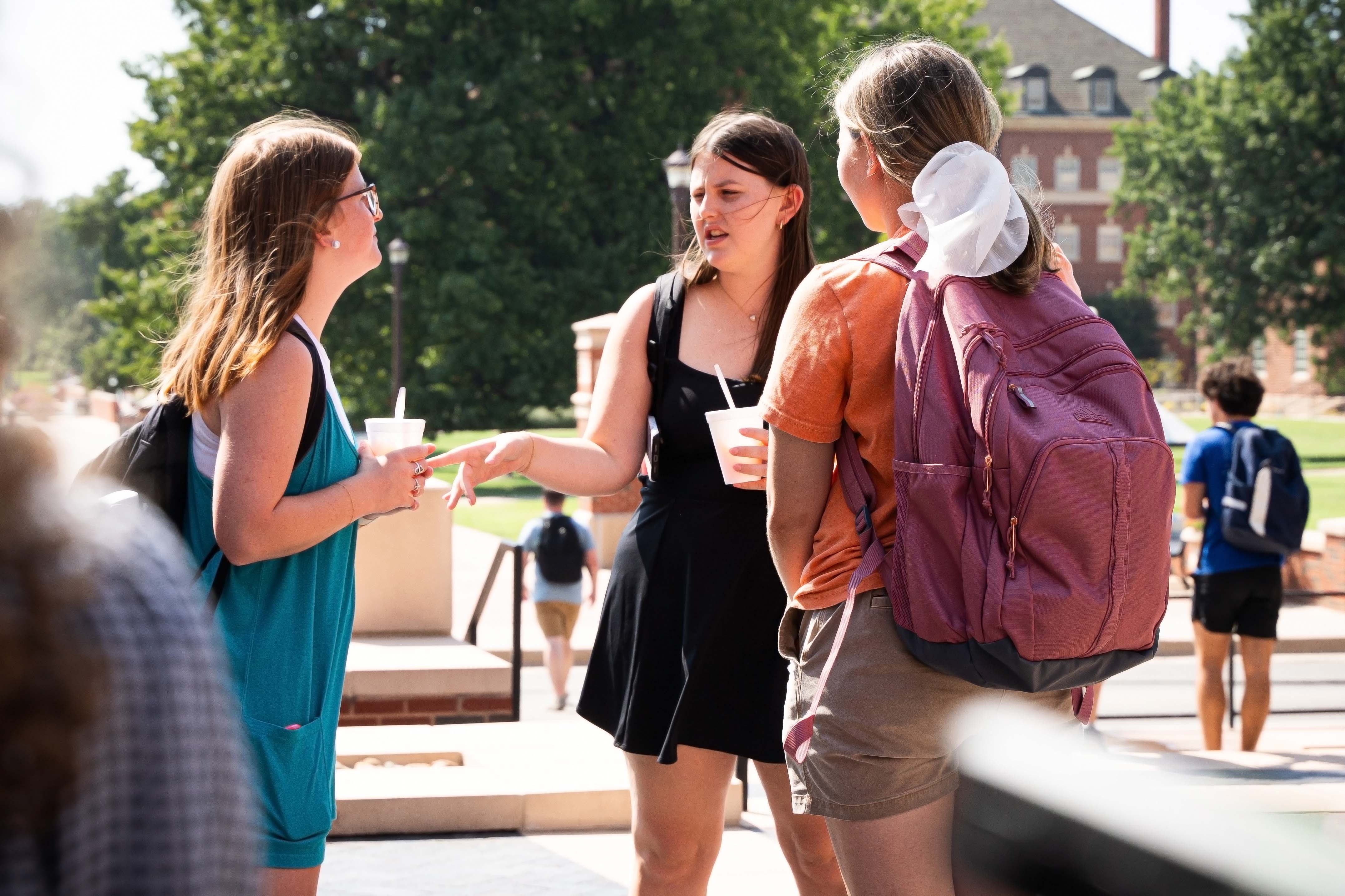 Three female students holding snow cones and talking in the Business Building courtyard.