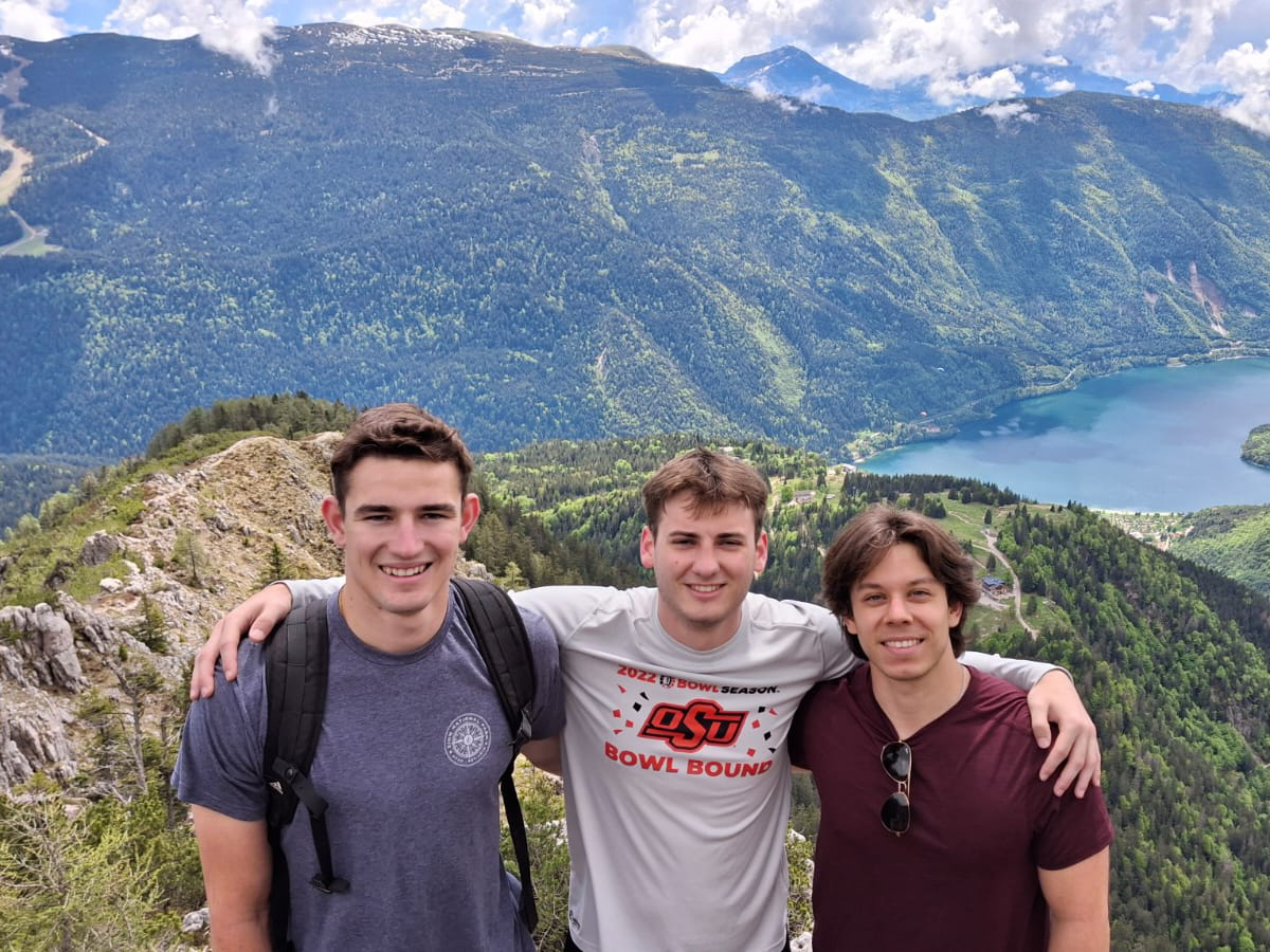 Three male student smile with a mountain view in the background.