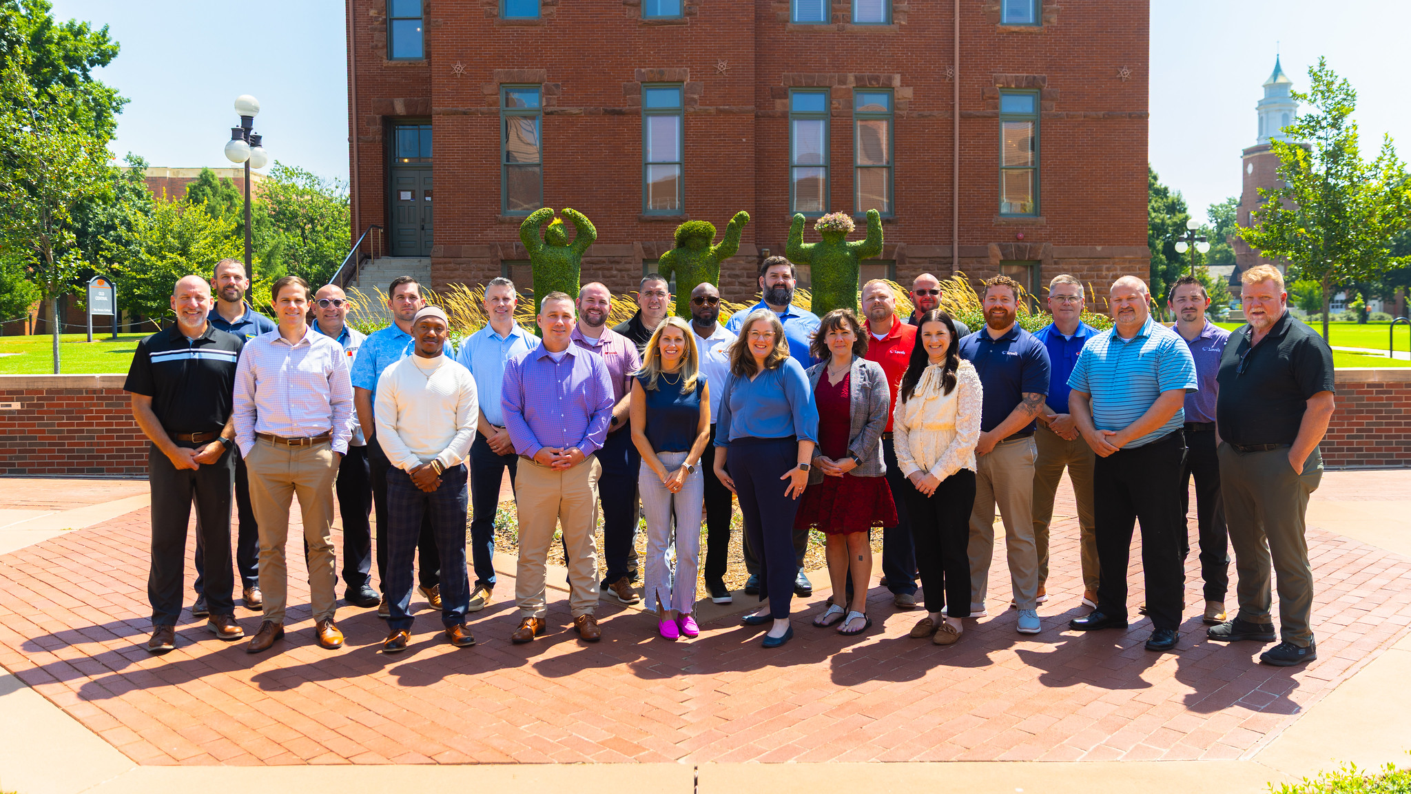 group of people standing outside in front of an OSU topiary