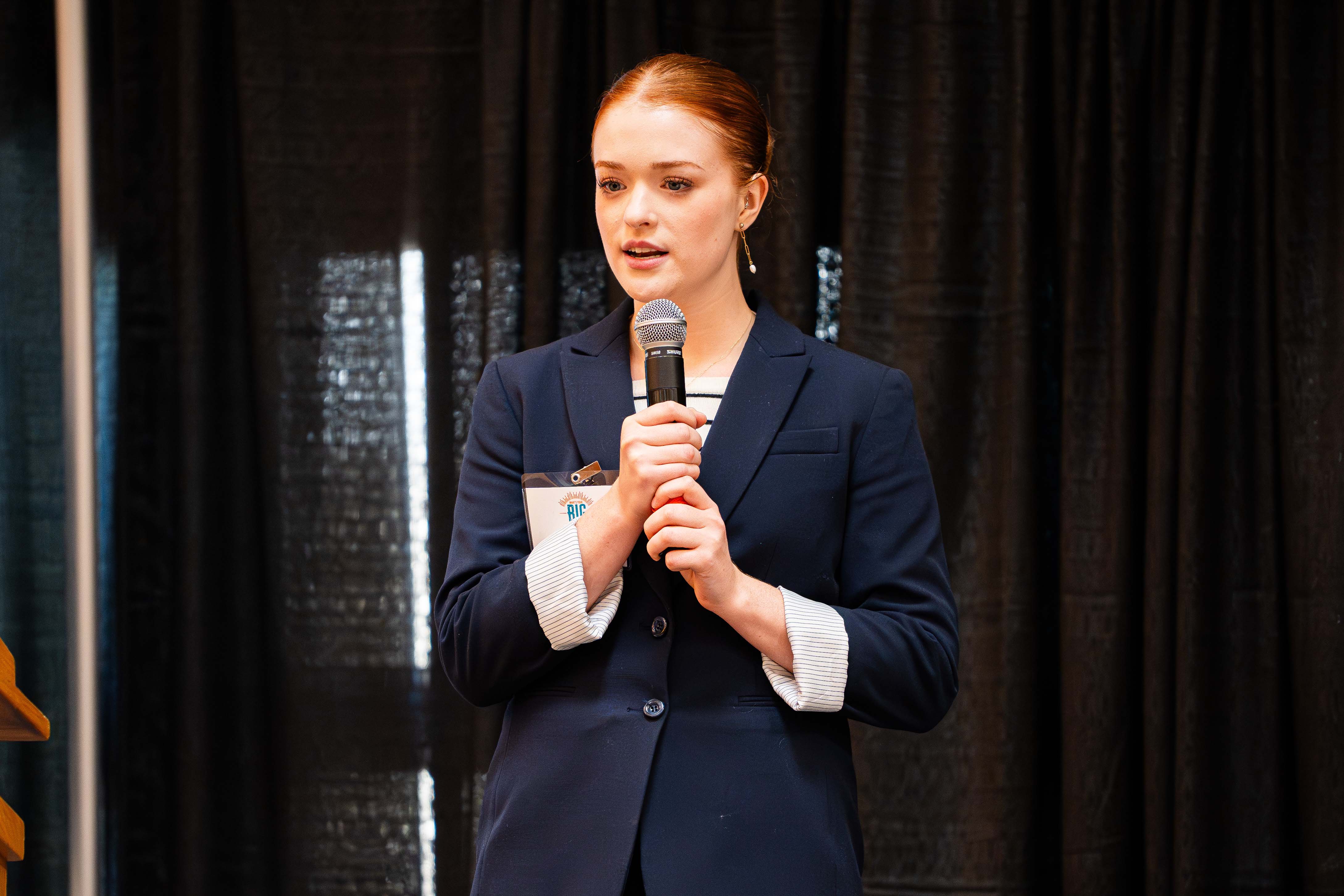 Female student dressed professionaly speaks into a microphone