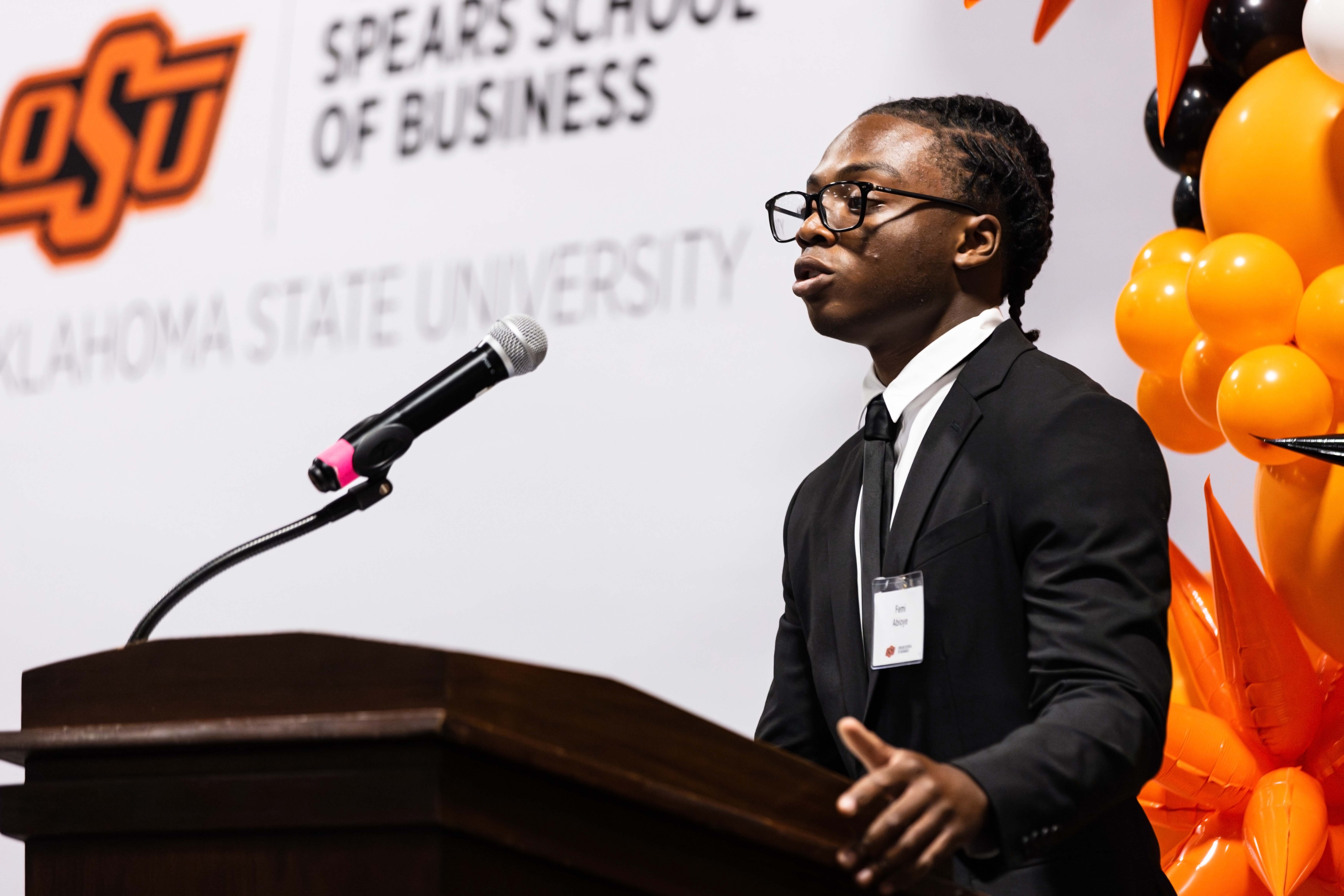 Male student speaking at a podium during the Scholarship Banquet wearing a black suit.