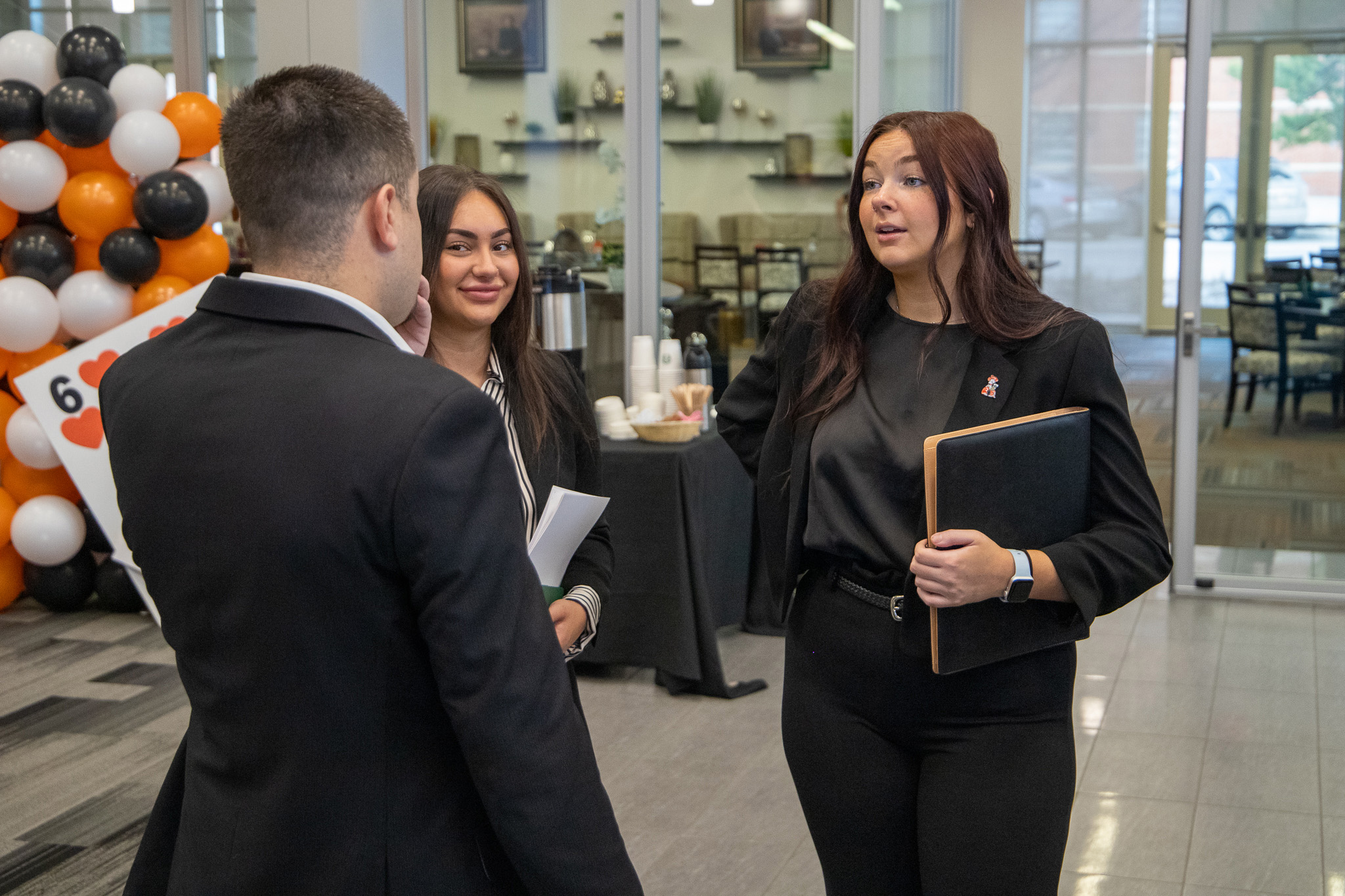 Two female students at Hospitality Days speaking with a male dressed in a suit.