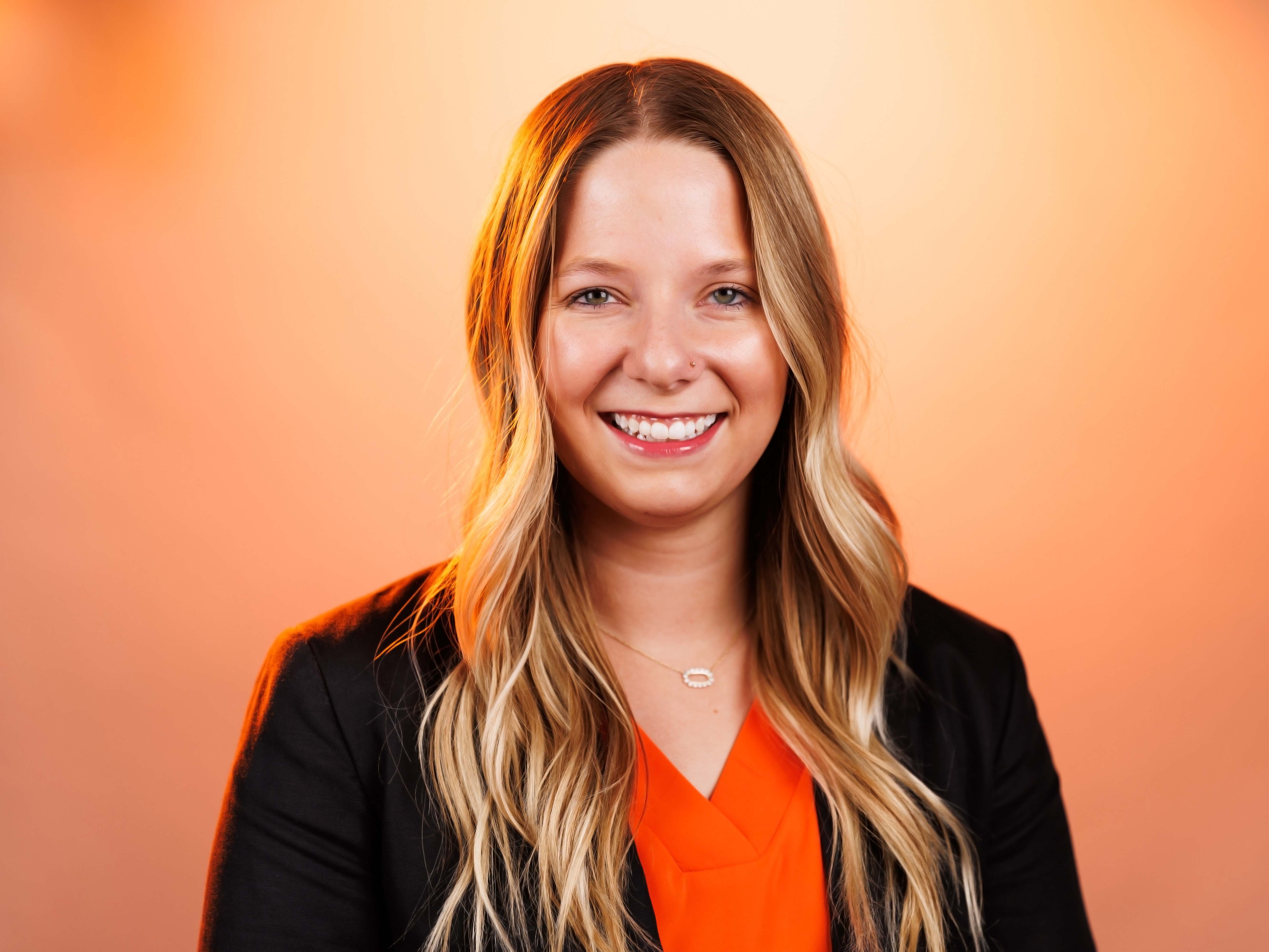 Headshot of Brie Barton with an orange background. Adam is wearing a suit.
