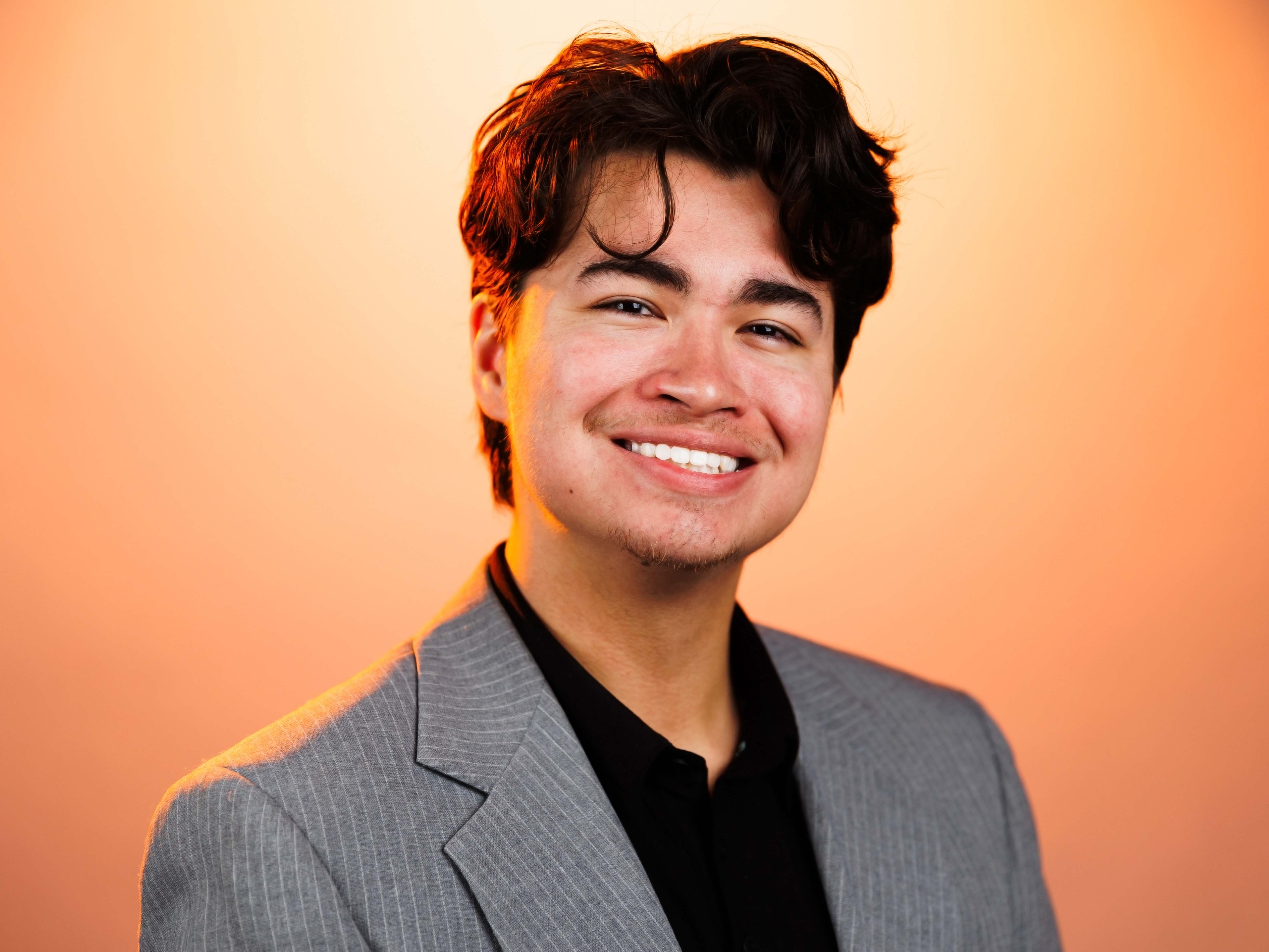 Headshot of Ike with an orange background. Ike is wearing a suit.