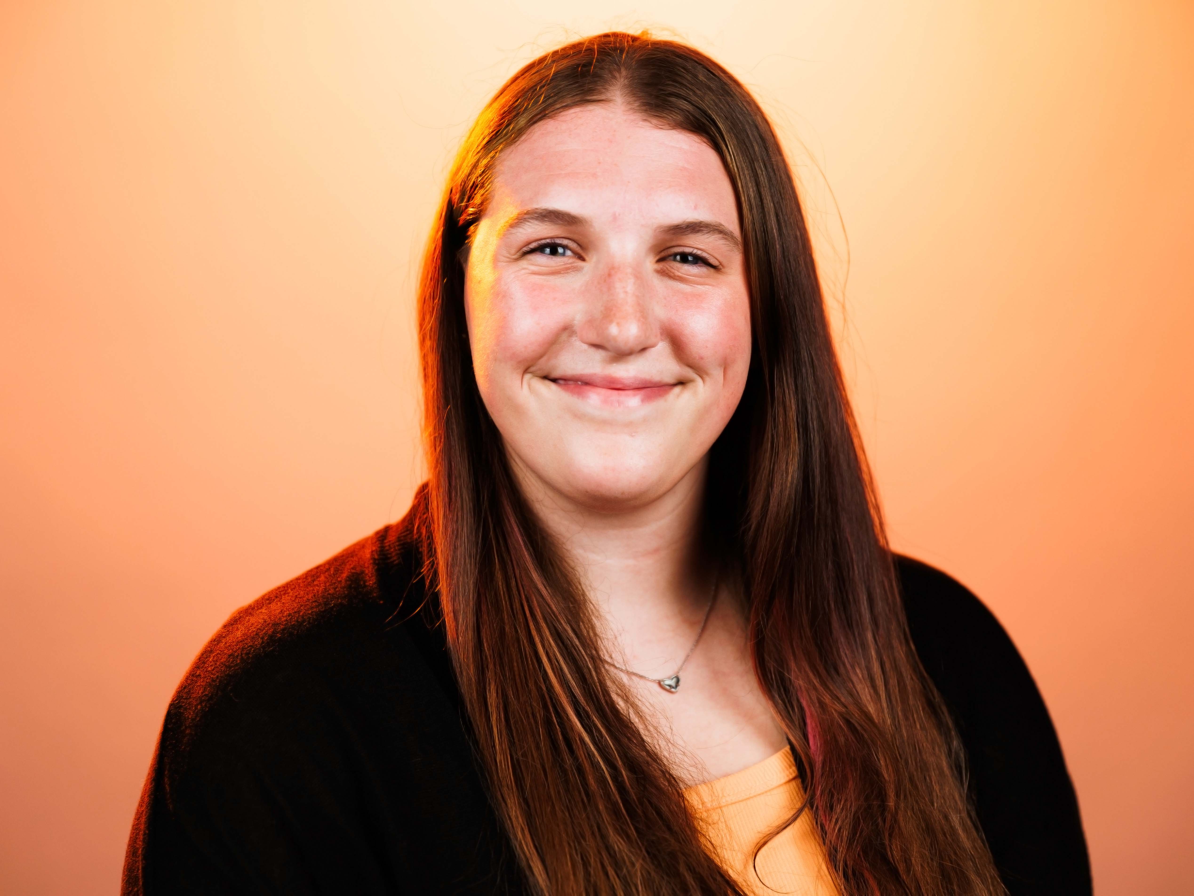 Headshot of Isabel with an orange background.