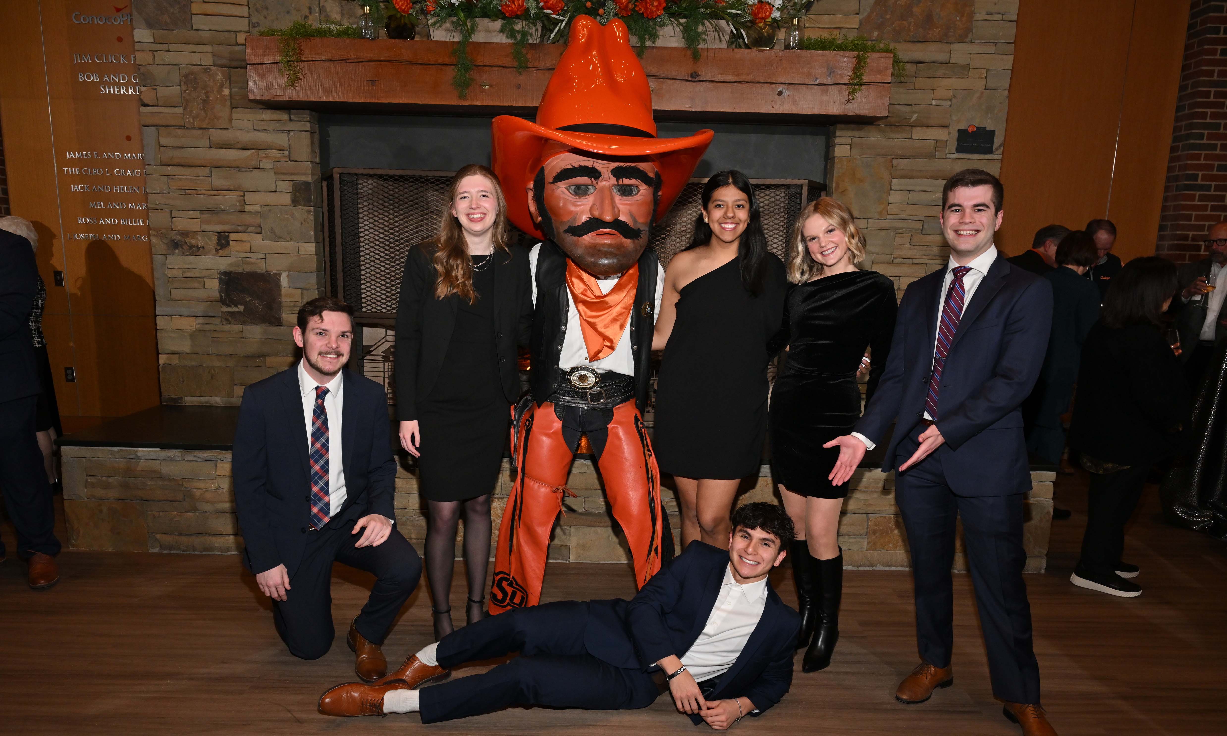Group of students in formal attire posing for a funny photo with the Pistol Pete mascot. One student laying on the groud propped up by his arm and smiling.