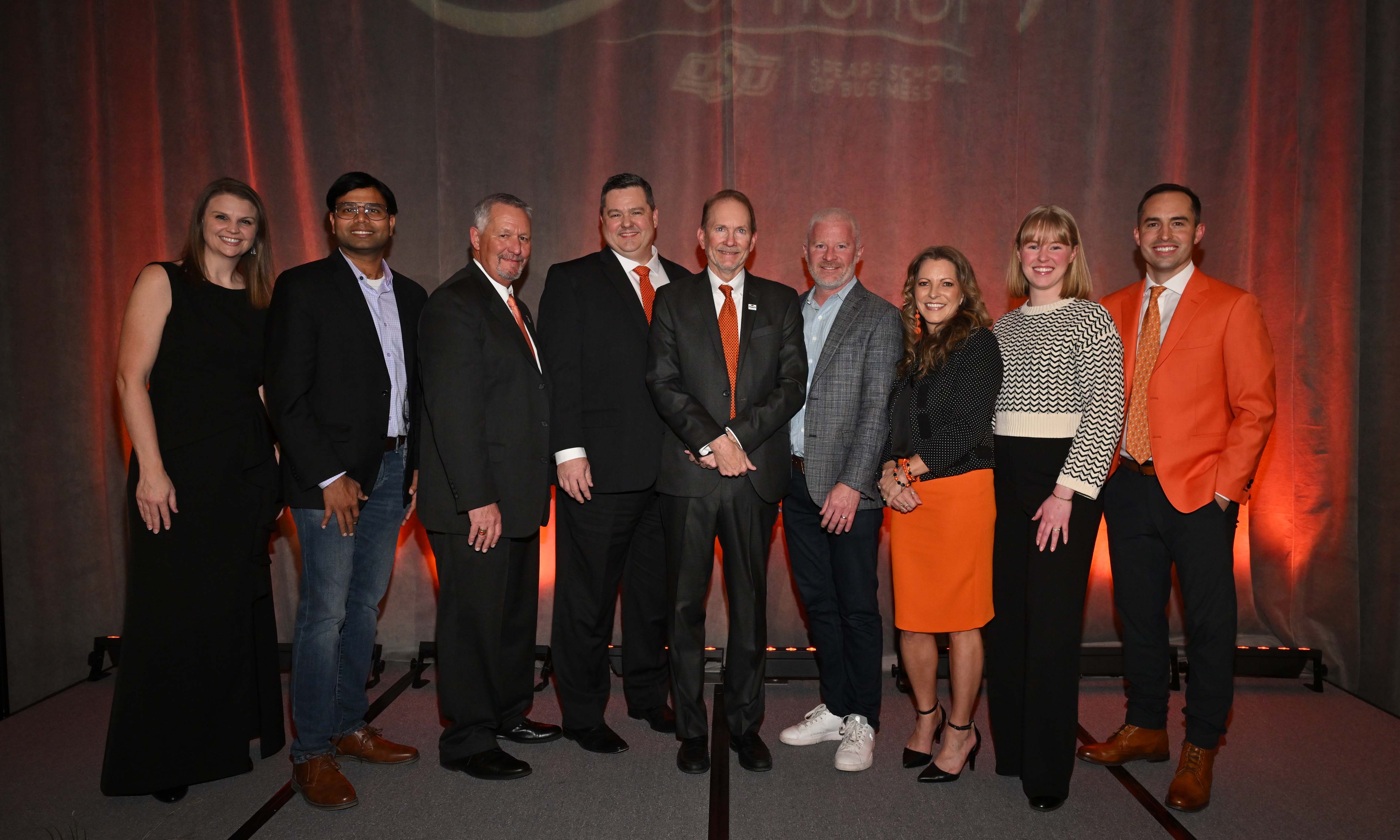 Group of alumni on a stage dressed in formal attire.