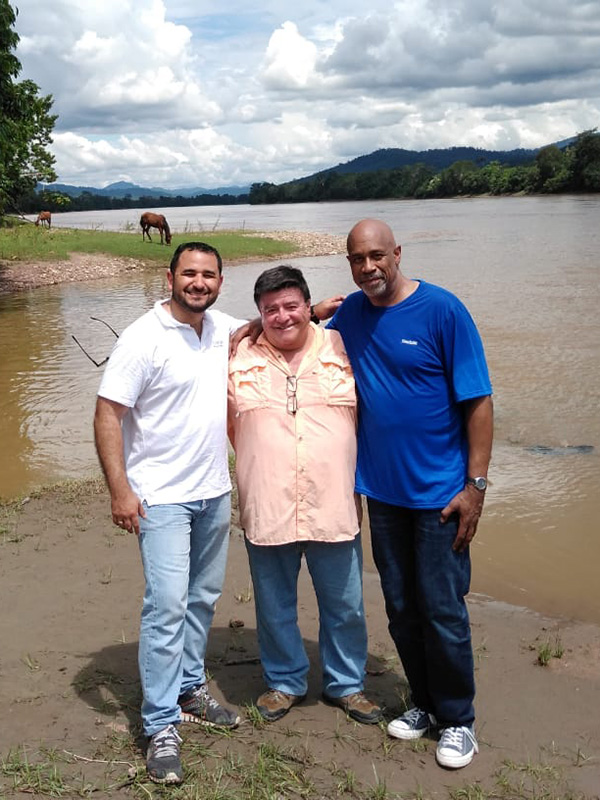 Group of three standling in front of a lake with mountains and horses behind them. This is alt text for the image