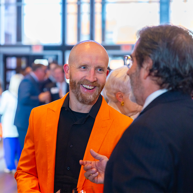 An honoree smiles while wearing a bright orange blazer.