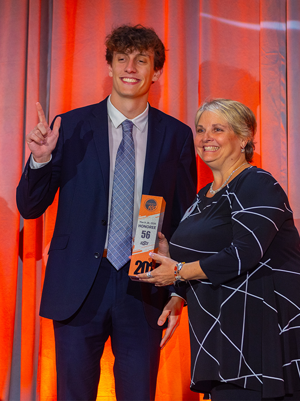 A Cowboy100 honoree poses with her award on stage with a male student in a suit.