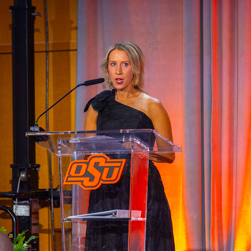 A woman speaking at the podium on the stage of the Cowboy100