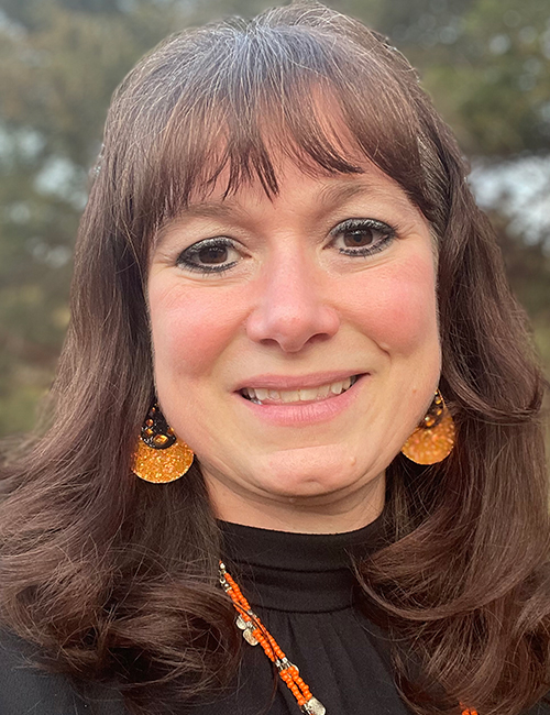 a smiling woman wearing a black top and orange jewelry