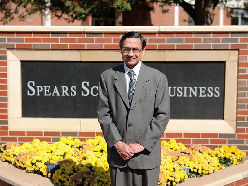 Spears sign Dr. Sharda stands in front of a Spears School of Business brick sign.
