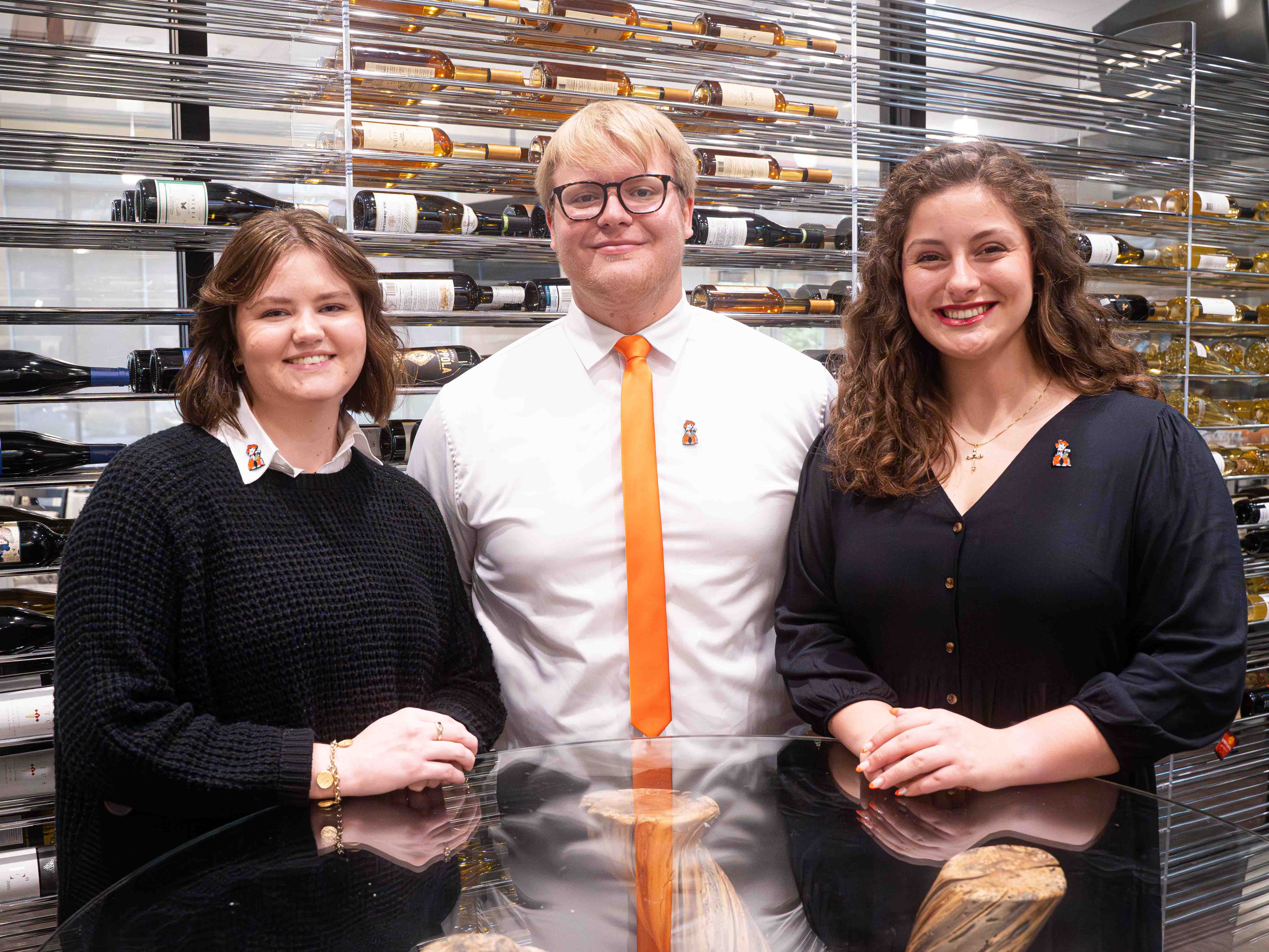 Three students smiling in front of wine display at the Hirst Center